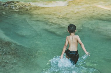 Bir nehir taşları tam dikkatle geçiş ve şelale Erawan Milli Parkı Kanvhanaburi, Tayland teetering küçük çocuk.