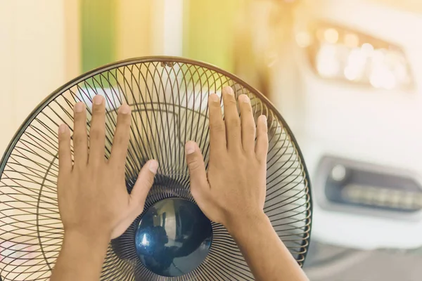 Hand of Young man touch and adjust  on front grills of electric fan for a good wind