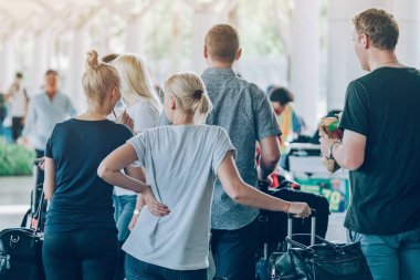 Büyük silindir bagajı olan yolcular, havaalanı varış terminalinden arabanın almasını beklemek için ayakta dururlar..