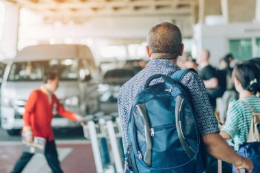 Büyük silindir bagajı olan yolcular, havaalanı varış terminalinden arabanın almasını beklemek için ayakta dururlar..