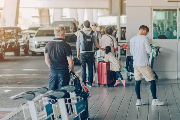 Pasażerowie z dużym bagażem stoją czekać na samochód odebrać w terminalu przylotów lotniska. — Zdjęcie stockowe
