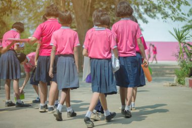 Mutluluğa geri dönüş ilkkız öğrencileri pembe gömlek ve mavi etek arkadaşlarıyla sınıflara yürüyor.