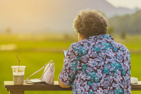 Mulher idosa se senta para descansar e espera por tempo para tirar fotos do pôr do sol — Fotografia de Stock