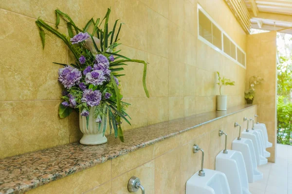 Konstgjorda blommor i krukor för dekoration placeras på hyllan ovanför urinoaren — Stockfoto