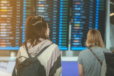 Uçuş bilgi tahtaslarına bakan ve uluslararası havaalanında uçuşlarını kontrol eden yolcular