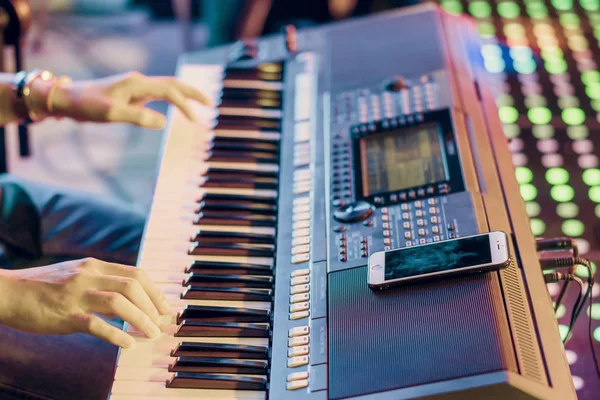 ミュージシャンは、コンサートのステージで演奏するためのガイドラインとしてスマートフォンを使用して電子キーボードシンセサイザーを再生します — ストック写真