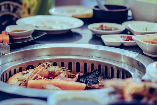 People grilling meat on a smokeless barbecue grill in a restaurant.