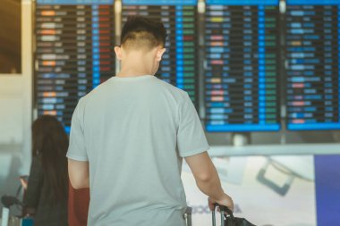 Uçuş bilgi tahtaslarına bakan ve uluslararası havaalanında uçuşlarını kontrol eden yolcular