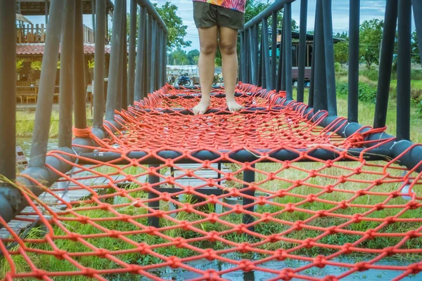 Ung kvinna försökte gå på bro golvet bunden med ett rött rep för att korsa träsket i fälten. — Stockfoto