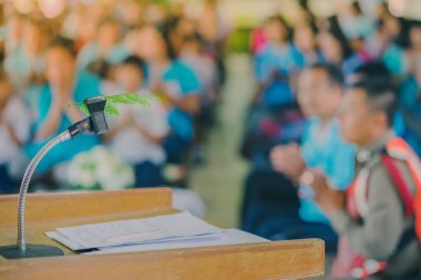 Okul konferans salonundaki podyumdaki masaüstü mikrofon standına yerleştirilmiş yapay yaprak.