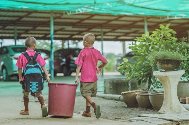 Erkek öğrenciler atık toplamak için sınıftaki çöpleri atmaya yardım ederler