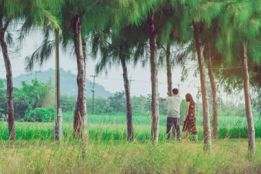 Halk parkındaki çam ağaçlarının altında yürüyen ve fotoğraf çeken çift..