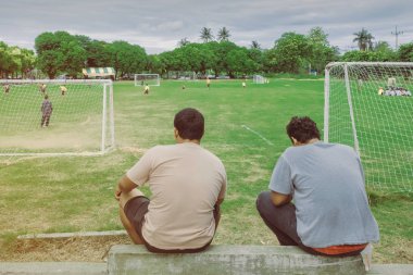 Erkek ebeveynlerin okulda futbol oynayan çocuklarına tezahürat geri görünümü.