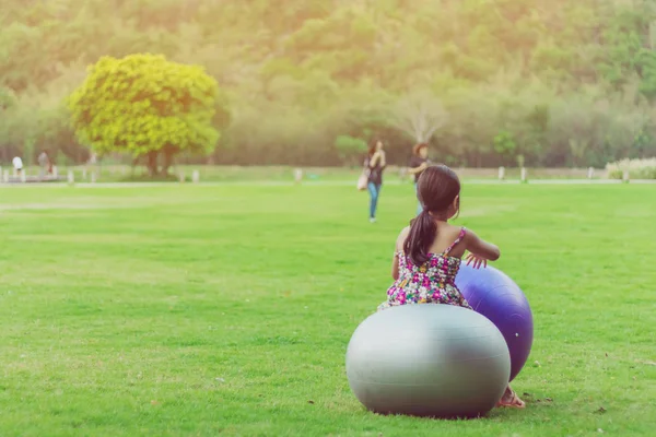 Menina felicidade na saia floral relaxar e jogar com uma grande bola no campo verde no jardim público . — Fotografia de Stock