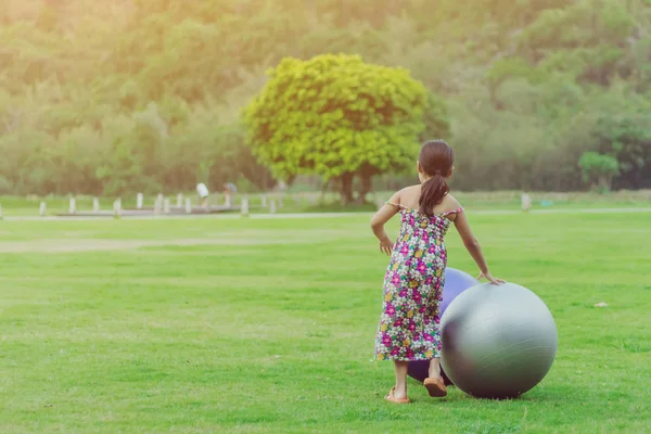 Glücksmädchen im Blumenrock entspannen sich und spielen mit einem großen Ball auf der grünen Wiese im öffentlichen Garten. — Stockfoto