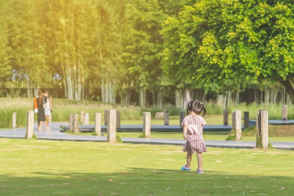 Ein kleines Mädchen im rosafarbenen Rock genießt eine entspannte Zeit beim Spielen auf dem grünen Rasen im öffentlichen Park am Abend. — Stockfoto