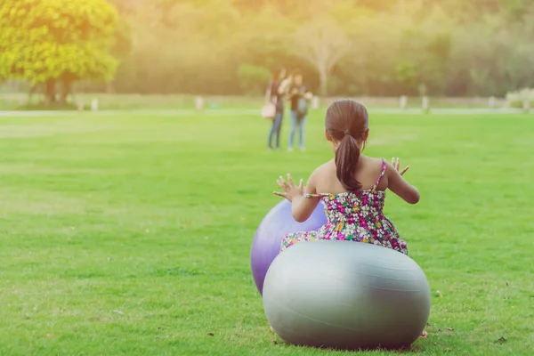 Glücksmädchen im Blumenrock entspannen sich und spielen mit einem großen Ball auf der grünen Wiese im öffentlichen Garten. — Stockfoto