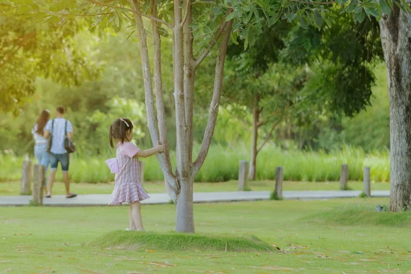 Una niña con una falda rosa disfruta de un tiempo relajante jugando en el césped verde en el parque público por la noche . — Foto de Stock