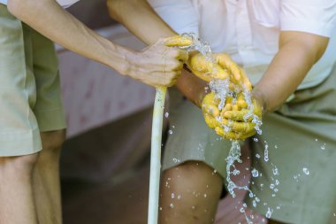 Sarı yağ rengi ile boyanmış elleri yıkamak için beyaz kauçuk tüpsu püskürtme bahçe hortumu tutan öğrenci.