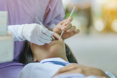 Dişçi, ağız aynası olan ve okulda araştırma yapan bir öğrencinin dişlerini inceliyor..