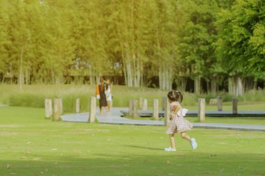 Pembe etekli küçük bir kız akşam ları parktaki yeşil çimenlikte oynarken dinlendirici bir zaman sahiptir..