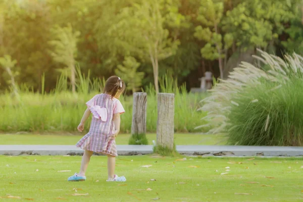 Una niña con una falda rosa disfruta de un tiempo relajante jugando en el césped verde en el parque público por la noche . — Foto de Stock