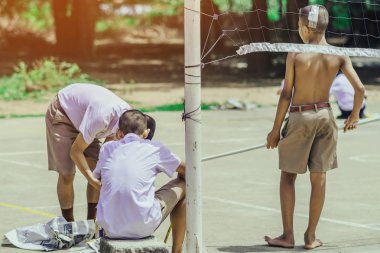 Erkek öğrenciler Sepak Takraw eğitimi için çimento zemin üzerinde sarı çizgiler boyamak için küçük boya silindirleri kullanın.