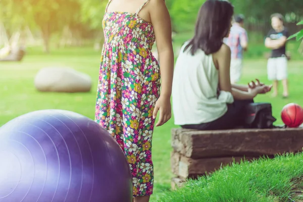 Dívka štěstí v květinové sukni relaxovat a hrát s velkou koulí na zeleném poli ve veřejné zahradě. — Stock fotografie