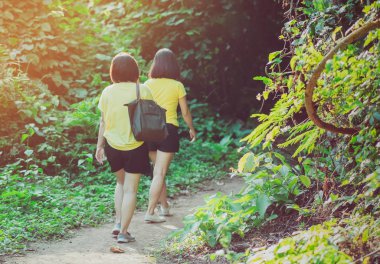 Mutluluğun arka planında aynı kıyafetleri giymiş iki kadın ormanda yürüyüş yolu boyunca yürüyorlar..