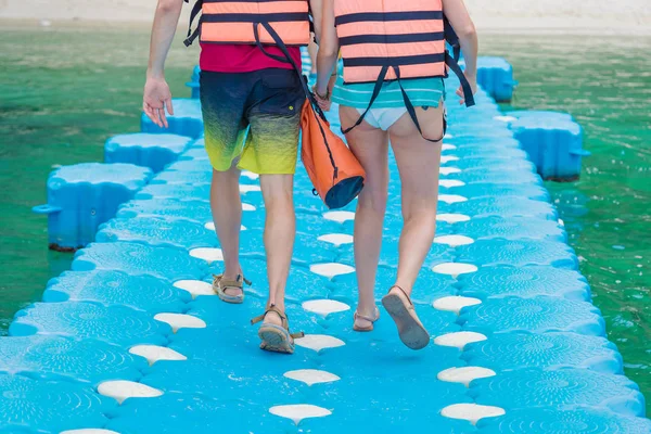 Milenci pár držící se za ruce při chůzi na plastovém pontonu chůze cesta plovoucí v moři jít na pláž. — Stock fotografie