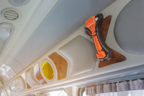 Orange safety glass hammer mounting near the window glass and curtain on the van for use to break the glass in case accident.