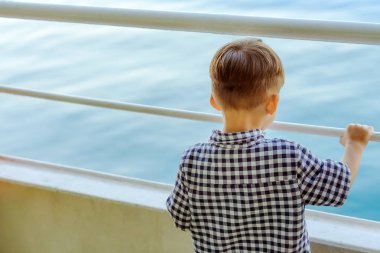 Asyalı çocuk feribot balyasında dinlenmek ve okyanusa ve adaya bakmak için duruyor.