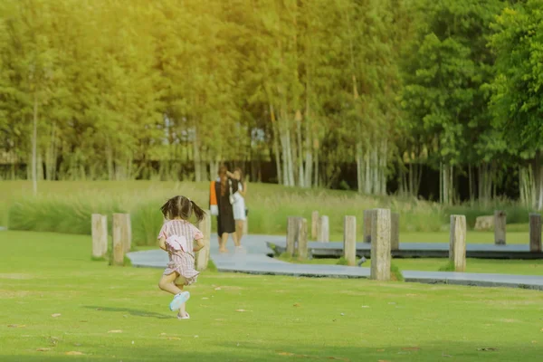 Ein kleines Mädchen im rosafarbenen Rock genießt eine entspannte Zeit beim Spielen auf dem grünen Rasen im öffentlichen Park am Abend. — Stockfoto