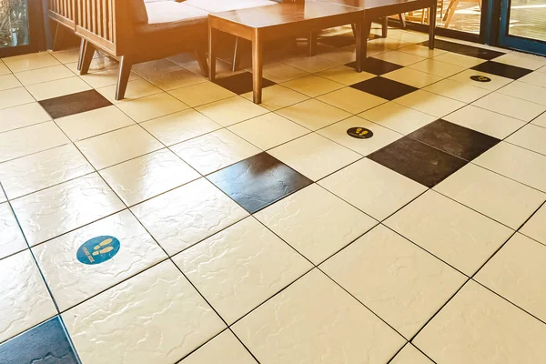 STAND HERE foot sign or symbol on the wooden floor in coffee shop. Coffee shop set foot sign for social distancing to order coffee and wait to take home.