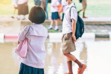 Coronavirus 'u (Covid-19) önlemek için yüz maskesi takan ilkokul öğrencisi, ailesinin okuldan sonra eve dönmesini bekler ve okul kapısının önünde yağmur durur.