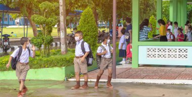 Kanchanaburi, Tayland-2 Temmuz 2020: Taylandlı öğrenciler okuldan sonra kendilerini Coronavirus 'tan (Covid-19) korumak ve KTR okulunda yağmur durduktan sonra evlerine dönmek için çeşitli tıbbi maskeler takıyorlar.