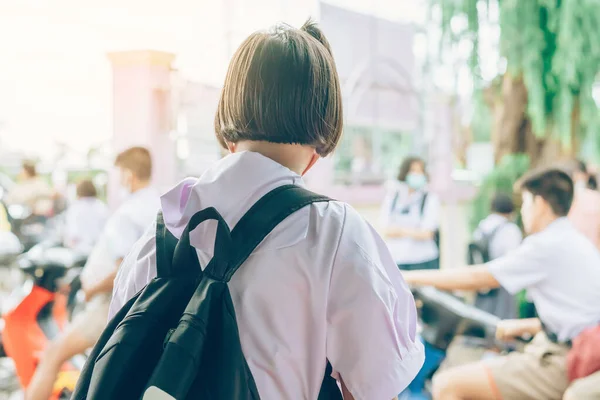 Female elementary school student wear face mask to prevent the Coronavirus(Covid-19) wait for her parents to pick her up to return home after school and the rain just stop in front of the school gate