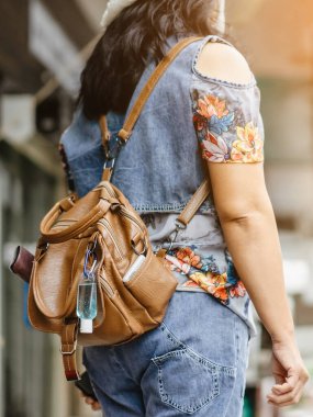 Corona Virüsü 'nü (Covid-19) öldürmek için mini taşınabilir alkol jeli şişesi şehirde dolaşırken maske takan bir kadının deri omuz çantasına asılır. Yeni normal yaşam tarzı. Alkol jeline odaklan