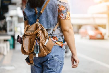 Corona Virüsü 'nü (Covid-19) öldürmek için mini taşınabilir alkol jeli şişesi şehirde dolaşırken maske takan bir kadının deri omuz çantasına asılır. Yeni normal yaşam tarzı. Alkol jeline odaklan