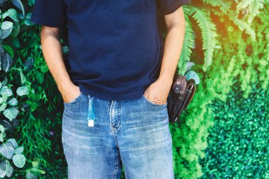 Corona Virüsü 'nü (Covid-19) öldürmek için Mini taşınabilir alkol jeli şişesi insan pantolonunun kemer düğümünde bitkisel arka planda asılı duruyor. Yeni normal yaşam tarzı. Sağlık hizmeti konsepti. Alkol jeline odaklan