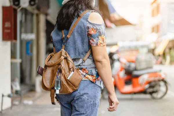 Mini portable alcohol gel bottle to kill Corona Virus(Covid-19) hang on a leather shoulder bag of a woman wearing a mask to travel in the city. New normal lifestyle. Selective focus on alcohol gel