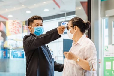 KANCHANABURI, THAILAND-11 Temmuz 2020: Güvenlik görevlisi, Robinson Mağazası girişinde Coronavirus 'u (Covid-19) önlemek için müşteriler için vücut termometresi ve alkol jeli enjeksiyon hizmetini kullanın