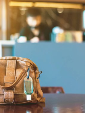 Corona Virüsü 'nü (Covid-19) öldürmek için mini taşınabilir alkol jeli şişesi kahve dükkanındaki kahverengi deri bir çantada asılı duruyor. Yeni normal yaşam tarzı. Sağlık hizmeti konsepti. Alkol jeline odaklan