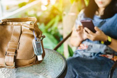 Corona Virüsü 'nü (Covid-19) öldürmek için taşınabilir mini alkol jeli şişesi bahçedeki masada kahverengi deri bir omuz çantasına asılır. Yeni normal yaşam tarzı. Sağlık hizmeti konsepti. Alkol jeline odaklan