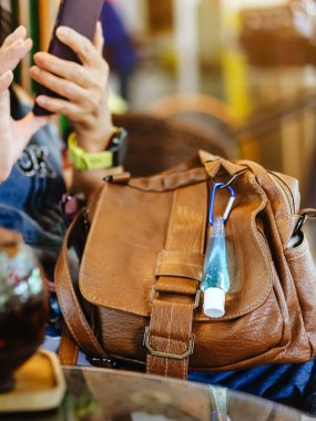 Corona Virüsü 'nü (Covid-19) öldürmek için mini taşınabilir alkol jeli şişesi kafede sıcak kahveli kahverengi deri bir omuz çantasına asılır. Yeni normal yaşam tarzı. Sağlık hizmeti kavramı. Alkol jeline odaklı.