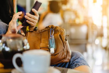 Corona Virüsü 'nü (Covid-19) öldürmek için mini taşınabilir alkol jeli şişesi kafede sıcak kahveli kahverengi deri bir omuz çantasına asılır. Yeni normal yaşam tarzı. Sağlık hizmeti kavramı. Alkol jeline odaklı.