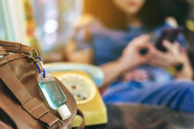 Corona Virüsü 'nü (Covid-19) öldürmek için mini taşınabilir alkol jeli şişesi kahve dükkanındaki kahverengi deri bir çantada asılı duruyor. Yeni normal yaşam tarzı. Sağlık hizmeti konsepti. Alkol jeline odaklan