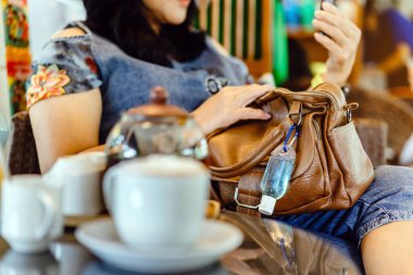 Corona Virüsü 'nü (Covid-19) öldürmek için mini taşınabilir alkol jeli şişesi kafede sıcak kahveli kahverengi deri bir omuz çantasına asılır. Yeni normal yaşam tarzı. Sağlık hizmeti kavramı. Alkol jeline odaklı.