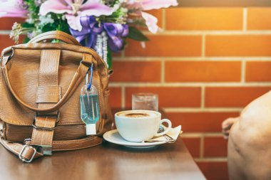 Corona Virüsü 'nü (Covid-19) öldürmek için mini alkol jeli şişesi kafede üzerinde sıcak kahve olan kahverengi deri bir omuz çantasına asılır. Yeni normal yaşam tarzı. Sağlık hizmetleri kavramı. Alkol jeline odaklanın.