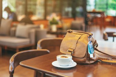 Corona Virüsü 'nü (Covid-19) öldürmek için mini alkol jeli şişesi kafede üzerinde sıcak kahve olan kahverengi deri bir omuz çantasına asılır. Yeni normal yaşam tarzı. Sağlık hizmetleri kavramı. Alkol jeline odaklanın.